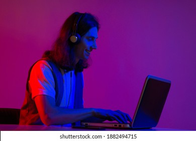 Online programming training, computer programmer or student. A young man with long hair and headphones. Use a laptop, neon tinting