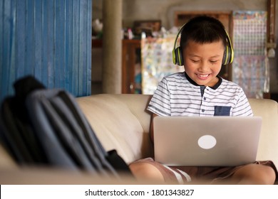 Online remote learning, distance education and homeschooling concepts. School kid Asian preteen boy in headphone using laptop computer on couch in rustic rural home during COVID-19 pandemic. - Powered by Shutterstock