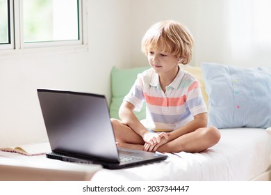 Online remote learning. School kid with computer having video conference chat with teacher and class group. Child studying from home. Little boy on bed with laptop and tablet. Coronavirus outbreak. - Powered by Shutterstock