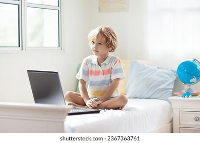 Online remote learning. School kid with computer having video conference chat with teacher and class group. Child studying from home. Little boy on bed with laptop and tablet.  - Shutterstock ID 2367363761