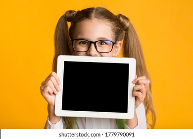 Online School App. Schoolgirl Showing Tablet Computer Empty Screen Over Yellow Background. Mockup, Studio Shot
