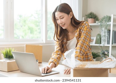 Online sell store, startup small business entrepreneur asian young woman using laptop computer check order purchase from web, owner working at home office, preparing pack product parcel for delivery. - Shutterstock ID 2394541131