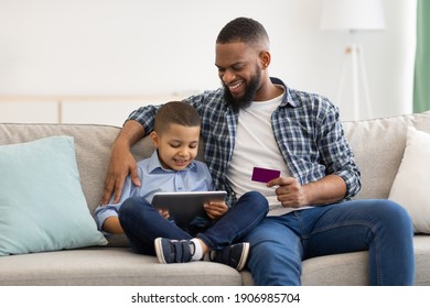 Online Shopping. Black Father And Son Using Digital Tablet Buying Things And Making Payment Via Credit Card Sitting On Couch At Home. Modern Family Shopping Concept - Powered by Shutterstock