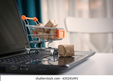 Online Shopping Concept. Shopping Cart, Small Boxes, Laptop On The Desk