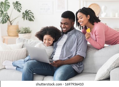 Online Shopping Concept. Cheerful Black Family Of Three Using Laptop And Credit Card At Home For Groceries Delivery Order