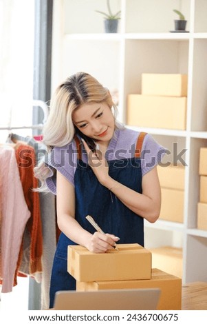 Online shopping concept, Female entrepreneur talks on smartphone and writes address on parcel boxes.