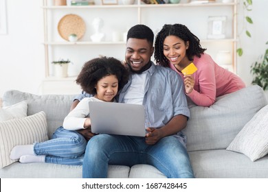 Online Shopping Concept. Happy African American Family With Little Daughter Using Laptop And Credit Card At Home For Buying Goods In Internet