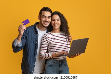 Online Shopping Concept. Happy Arabic Couple Using Credit Card And Laptop While Standing Over Yellow Background In Studio, Cheerful Middle Eastern Man And Woman Enjoying Purchasing In Internet - Shutterstock ID 2130810887