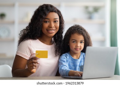 Online Shopping Concept. Happy Black Woman And Her Daughter Using Credit Card And Laptop To Buy Goods On Web From Home. Millennial Mom With Her Child Purchasing Stuff On Internet