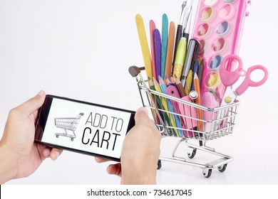 Online Shopping Concept, A Smartphone With Add To Cart Text And Shopping Cart Icon On A Mobile Phone With School Stationery In A Shopping Cart On Background