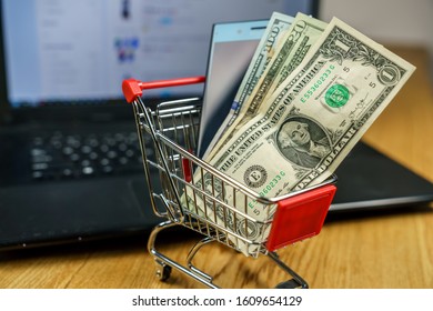 Online shopping concept. A smartphone and dollar banknotes in a trolley in front of a PC