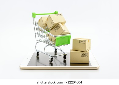 Online shopping and e commerce with delivery service concept : Small metal shopping cart and paper boxes or cartons, three in a basket and two fall outside, all are on a white gold smart mobile tablet