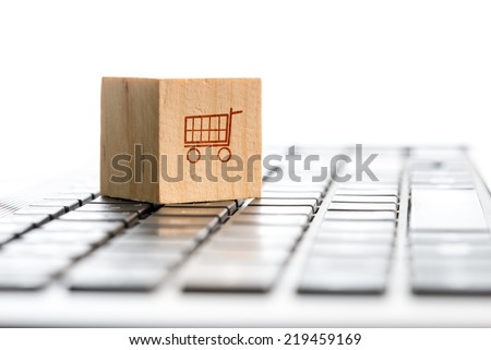 Online shopping and e-commerce concept with a wooden block with an icon of a shopping cart standing on a computer keyboard, viewed low angle with copyspace.