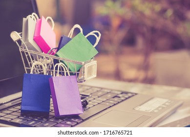 Online shopping  e-commerce and customer experience concept : Shopping bags and a shopping cart on a laptop keyboard, depicts consumers  buyers buy or purchase goods and service from home or office