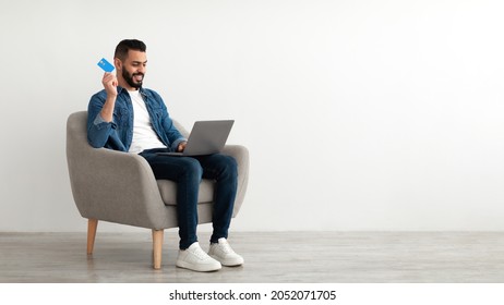 Online Shopping, E-commerce, Remote Banking. Young Arab Man Sitting In Armchair With Laptop, Using Credit Card To Purchase Goods On Web, Buying Products In Internet Store, Copy Space. Banner Design