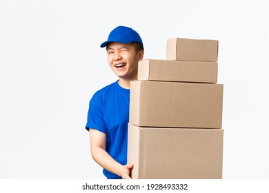Online shopping, fast shipping concept. Cheeky smiling asian courier in blue uniform holding boxes with client orders, wink friendly at customer, provide fast delivery, standing white background