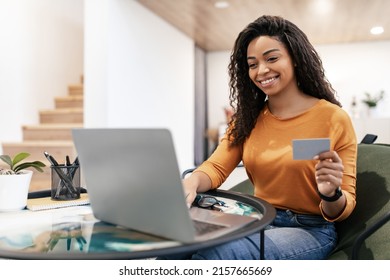 Online Shopping. Happy Black Woman Using Pc Laptop And Credit Card Making Payment Using Internet Banking Sitting On Chair At Home. Female Customer Paying With Bankcard Ordering Delivery On Website