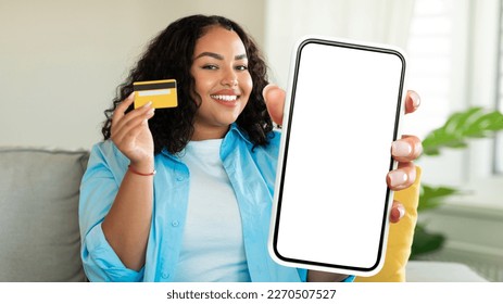 Online Shopping. Happy Black Woman Showing Blank Smartphone With White Screen And Holding Credit Card While Sitting On Couch At Home, Smiling Female Recommending App For Internet Purchases, Mockup - Shutterstock ID 2270507527