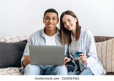 Online Shopping. Happy Positive Mixed Race Family Couple Sitting On A Sofa In Cozy Living Room, Using Laptop And Credit Card For Online Shopping, Buying Things For Home, Order Home Delivery, Smiling