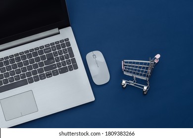 Online Shopping. Laptop With Pc Mouse, Supermarket Trolley On Classic Blue Background. Color 2020. Top View.