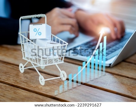 Online shopping purchase, sales increase, market trends concepts. Rising arrow on business growth graph near the shopping cart trolley with parcel boxes on desk near person using laptop computer.