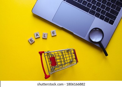 Online shopping and SALE concept. Grocery cart, laptop, word SALE made from wooden letters and magnifier on a yellow background. Discounts, season sales and black friday concept. Top view, flat lay - Powered by Shutterstock