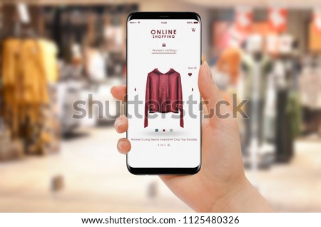 Online shopping with smartphone, clothing store in background