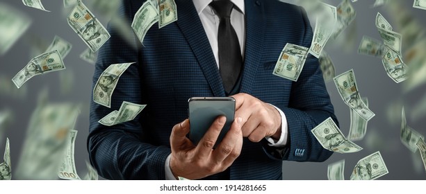 Online sports betting. A man in a suit is holding a smartphone and dollars are falling from the sky. Creative background, gambling - Shutterstock ID 1914281665