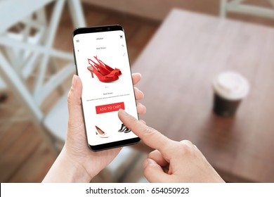 Online Store App Use On Modern Mobile Phone With Round Edges. Woman Touch Add To Cart Button For Red Shoes.