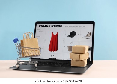 Online store. Laptop, mini shopping cart and purchases on beige table against light blue background - Powered by Shutterstock