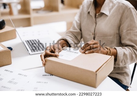 Online store owner sticking a barcode label onto a package box. Unrecognisable businesswoman preparing an order for shipping in a warehouse. Female entrepreneurs running an e-commerce small business.