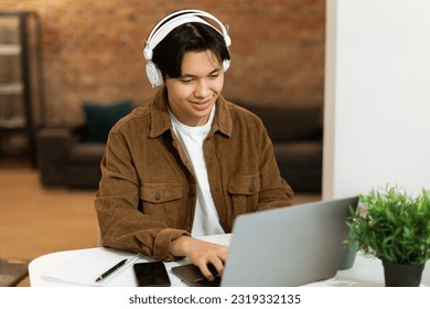 Online Study. Cheerful korean teenage guy using laptop computer, typing on keyboard during remote class at home. Boy at desk surfing web and learning, doing his homework indoors - Powered by Shutterstock