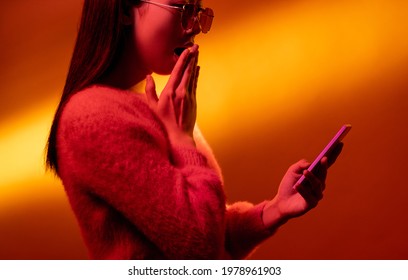 Online surprise  Neon light people  Mobile application  Pink color profile portrait amazed shocked Asian girl reading message and wow phone golden gradient copy space 