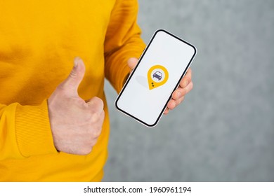 Online Taxi On Your Phone. A Man Holds A Smartphone With A White Screen And A Geolocation Icon And Shows A Thumbs Up