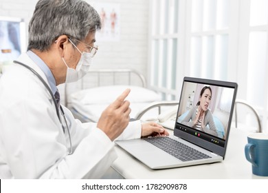 Online Tele Medicine Concept - Asian Senior Male Doctor With Face Mask Has Video Chat To Patient By Laptop In Hospital