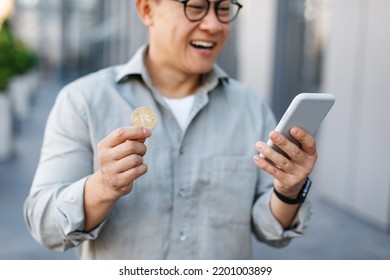 Online Trading. Happy Asian Man Holding Golden Bitcoin And Smartphone, Middle Aged Male Earning Cryptocurrency, Walking Outdoors In The City