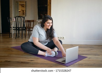 Online Training, Active Lifestyle And Vitality. Happy Sporty Girl With Curvy Body Using Laptop Being Strongly Motivated By Fitness Instructor On Video Lesson, Going To Exercise On Mat At Home