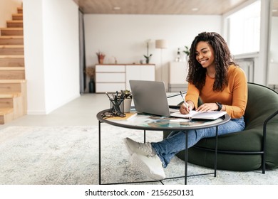 Online Training Concept. Smiling Casual Black Lady Sitting At Tea Coffee Table Working On Pc Laptop Writing Letter In Paper Notebook, Taking Notes Watching Weninar, Free Copy Space, Full Body Length