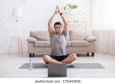 Online training with gadgets. Guy with smart watch doing yoga, watching training video at home in living room in daytime, free space