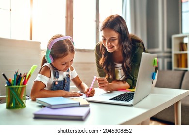 Online training. Mom helps her daughter with lessons. Schoolgirl in headphones listens to a lesson on a laptop. School at home in a pandemic and quarantine. - Powered by Shutterstock