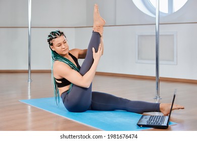 Online training of pole dancing, mature woman warms up and stretches while looking at laptop screen. - Powered by Shutterstock