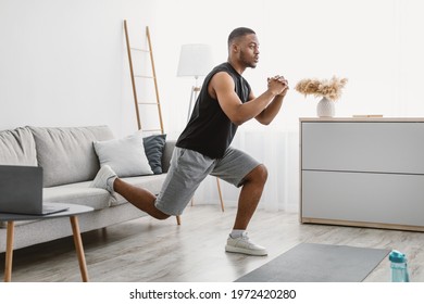 Online Training. Sporty Black Guy Doing Single-Leg Squats Near Couch Exercising At Laptop Computer During Workout At Home. Domestic Male Fitness And Sporty Lifestyle. Side View - Powered by Shutterstock