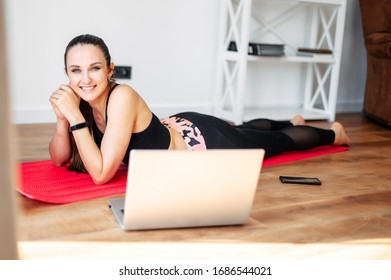 Online training, online video tutorial. A young woman in sportswear is using a laptop to watching workout video tutorial at home.