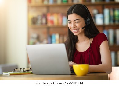 Online Tutoring. Smiling Asian Woman Tutor With Headset Working On Laptop In Cafe, Having Web Conference With Students