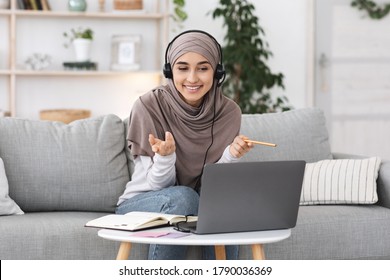 Online Tutoring. Young muslim woman teacher having video call with students, talking at laptop camera, sitting on couch at home