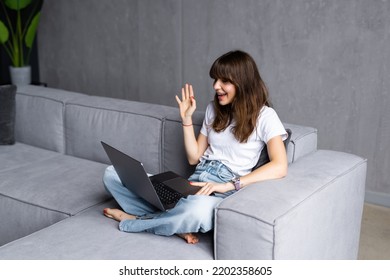 Online Video Call And Communication. Portrait Of Smiling Lady Using Laptop For Virtual Conference, Talking With Friends Or Family Waving Hand To Webcam, Cheerful Casual Female Sitting On Couch At Home