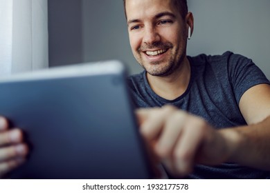 Online Video Chat. A Man With White Wireless Headphones In His Ears Is Talking To Friends Via Social Media On Grey Digital Tablet. Digital Age, New Normal, Stay Connected