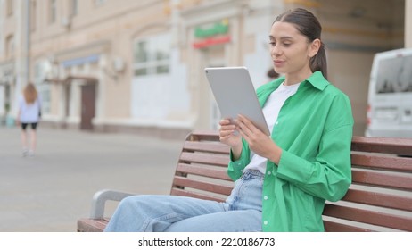 Online Video Chat On Tablet By Hispanic Woman Sitting Outdoor On Bench