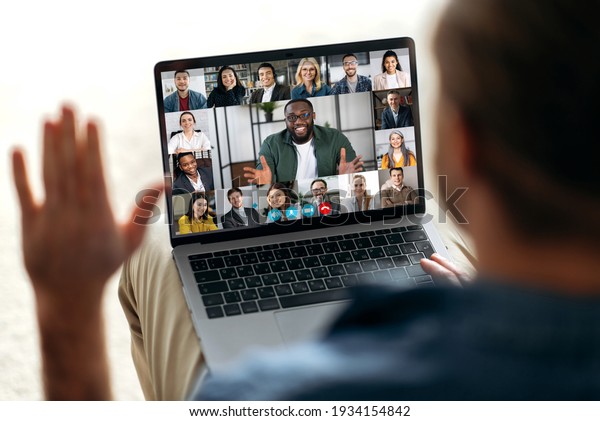 Online video communication concept. Over\
shoulder view at a laptop screen with different people, employees,\
business partners, guy greets colleagues, online briefing,\
brainstorming, group\
teleworking