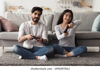 Online Video Game, Have Fun Together At Home, Domestic Entertainment At Spare Time. Happy Millennial Arab Female And Guy With Joysticks Play On Computer, On Floor In Living Room Interior, Copy Space